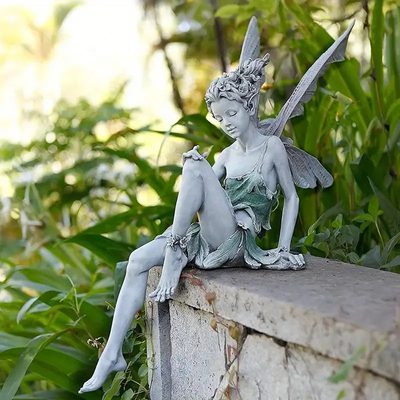 Statue of a fairy sitting on a stone ledge with greenery in the background